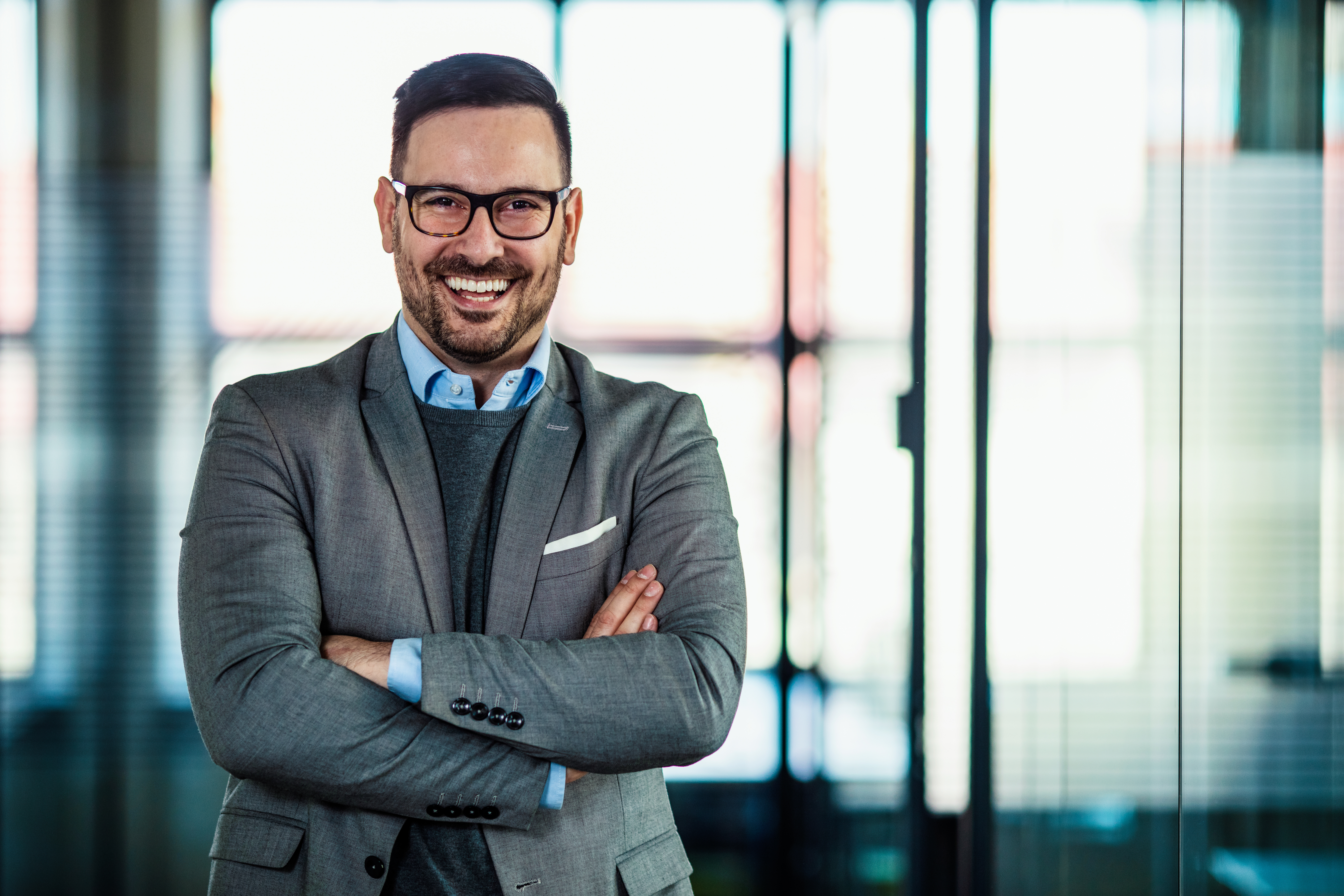 Portrait of a smiling businessman. Portrait of cheerful businessman with arms folded standing in conference room. Happy young business man looking at camera. Portrait of a smiling businessman in modern office with copy space.